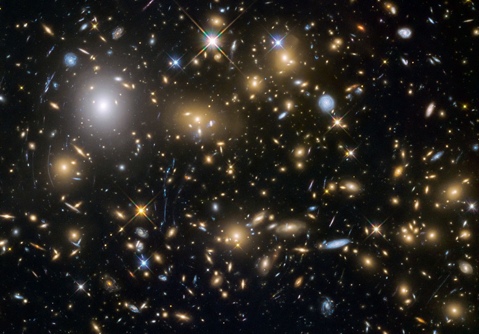 This image from the NASA/ESA Hubble Space Telescope shows the galaxy cluster MACSJ0717.5+3745. This is one of six being studied by the Hubble Frontier Fields programme, which together have produced the deepest images of gravitational lensing ever made. Due to the huge mass of the cluster it is bending the light of background objects, acting as a magnifying lens. It is one of the most massive galaxy clusters known, and it is also the largest known gravitational lens. Of all of the galaxy clusters known and measured, MACS J0717 lenses the largest area of the sky.